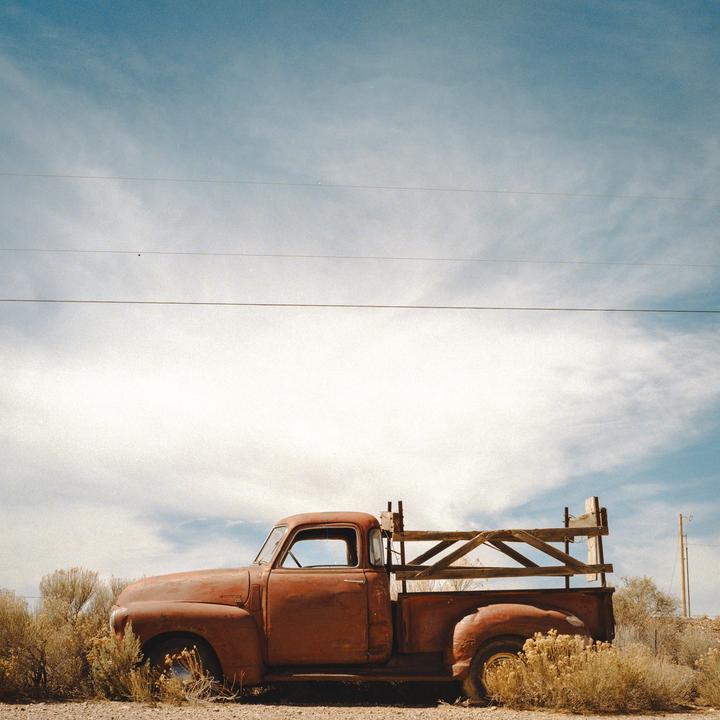 An old rusty pickup truck is parked on the side of a road under a partly cloudy sky.