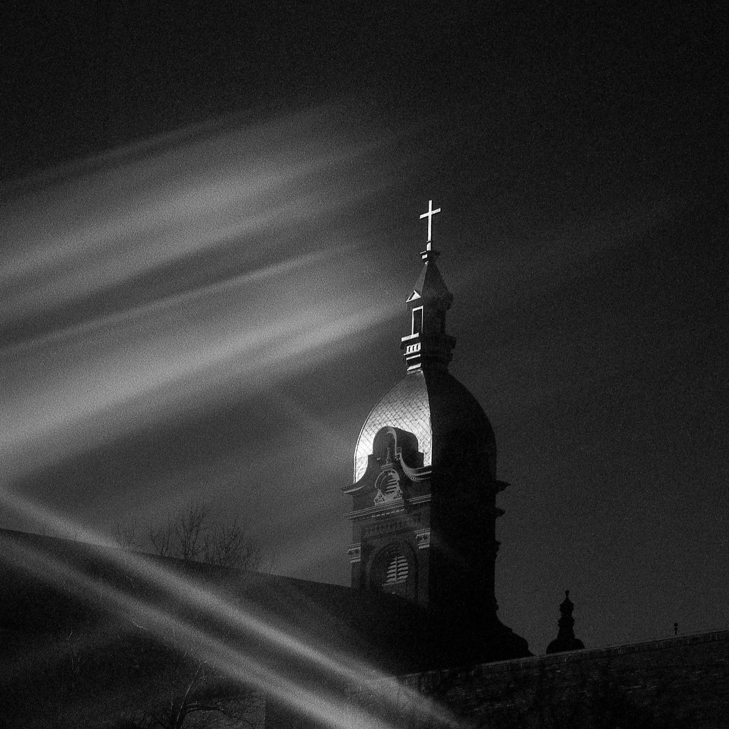 A church steeple with a cross on top is illuminated by spotlights at night.