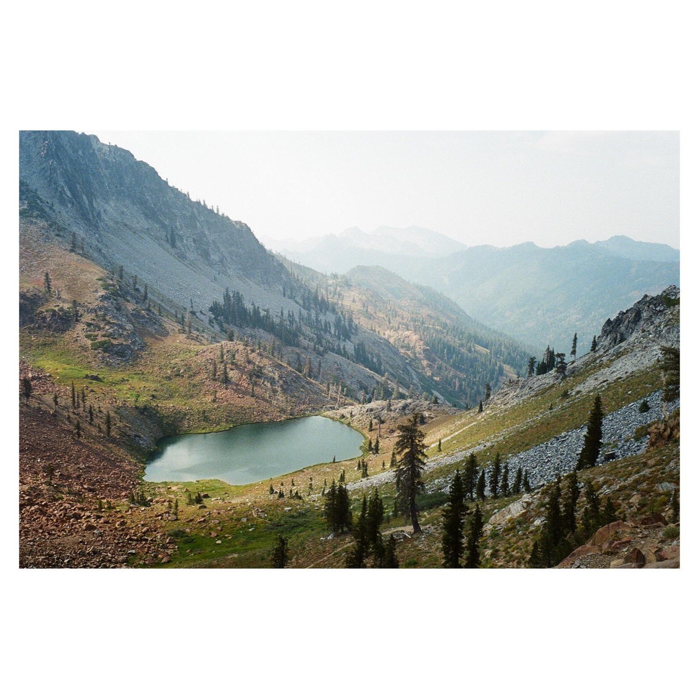 A small lake is nestled in a valley surrounded by mountains and pine trees.