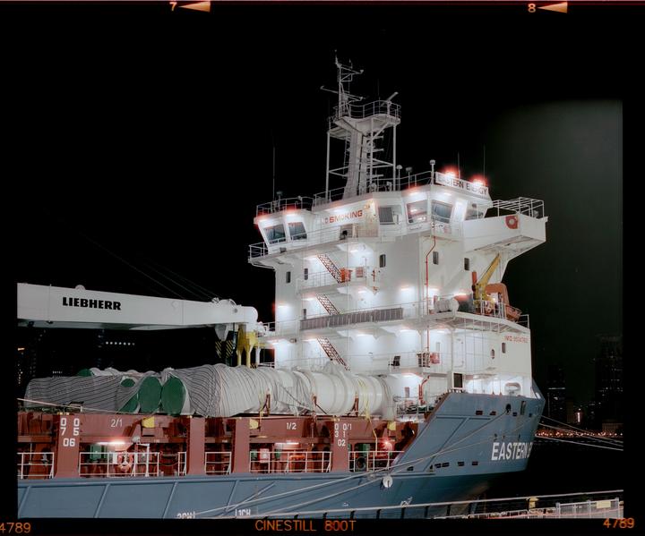 A large cargo ship with a crane is docked at night, illuminated by its own lights.