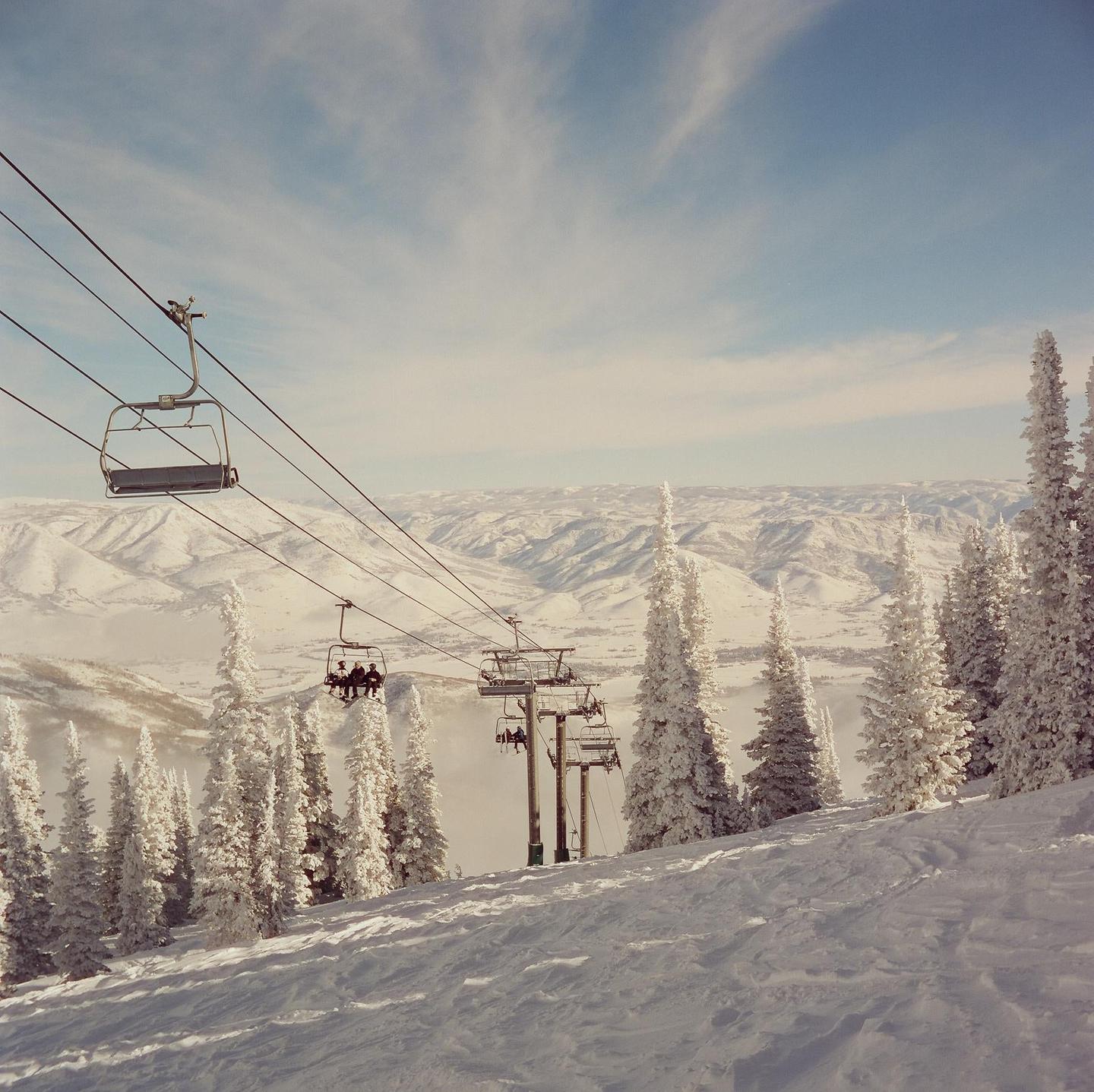 A ski lift carries people over a snowy mountain landscape with frosted trees.