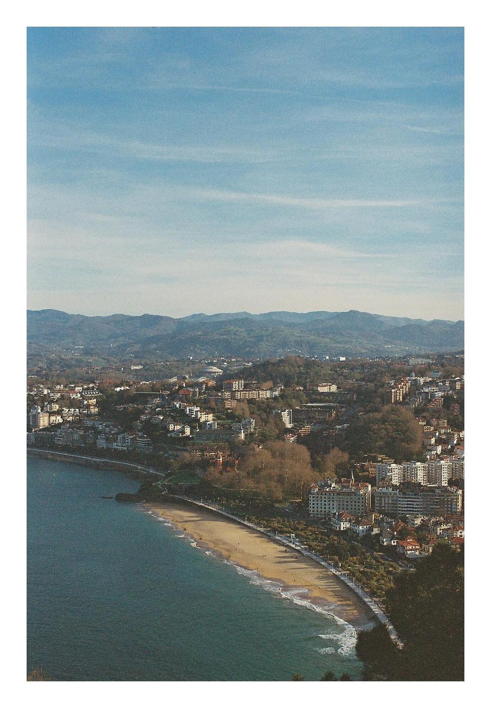 A city with a beach and mountains in the background is visible from an elevated perspective.