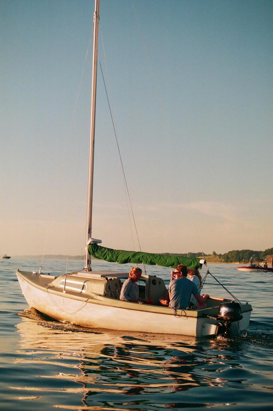 A small sailboat with four people on board moves across the water at golden hour.