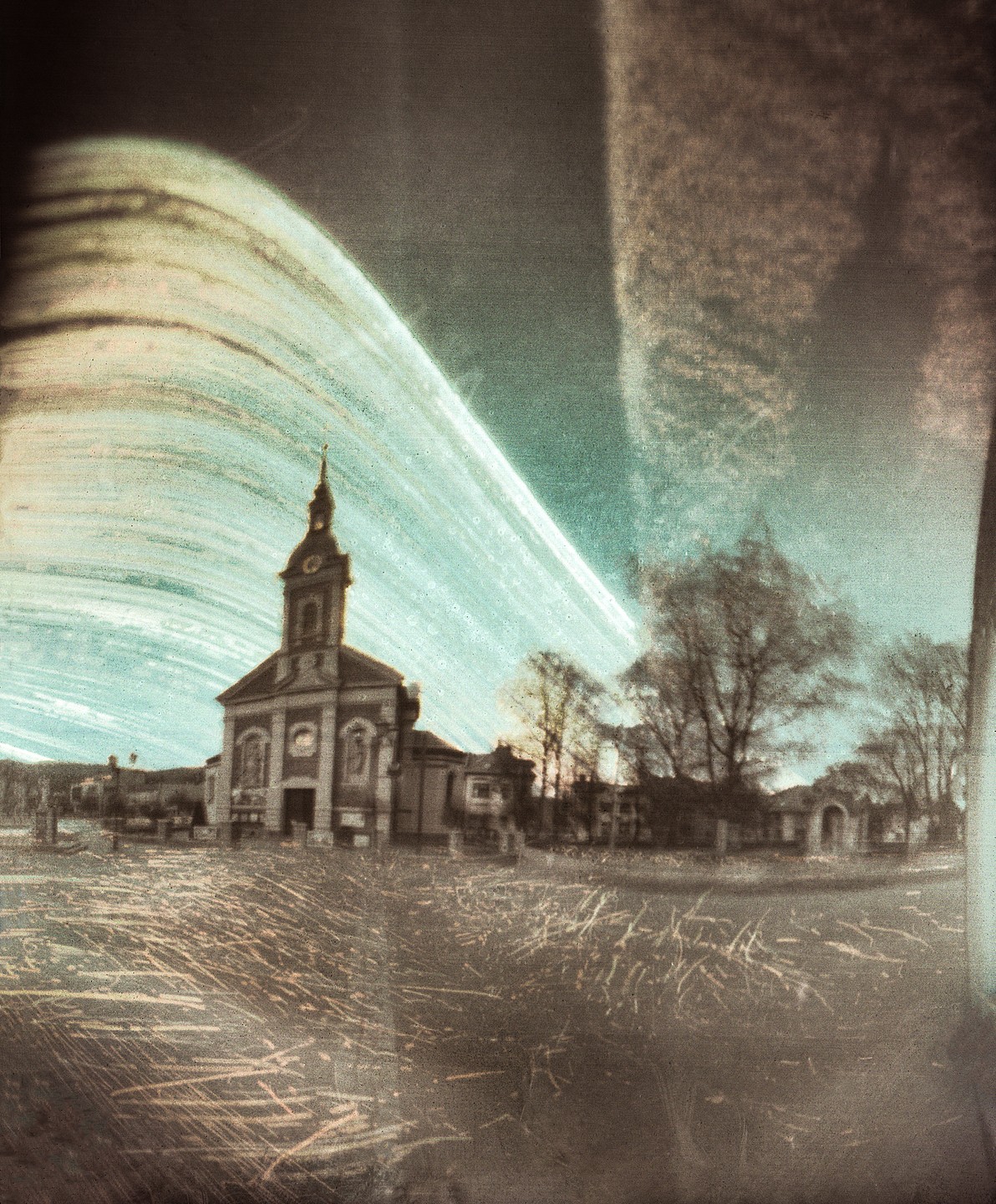 A church with a tall steeple stands in a town square under a streaked sky.