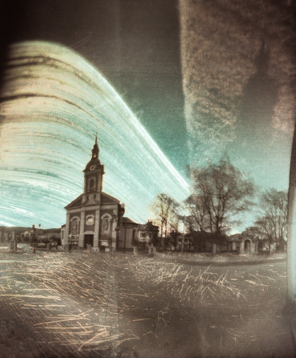 A church with a tall steeple stands in a town square under a streaked sky.