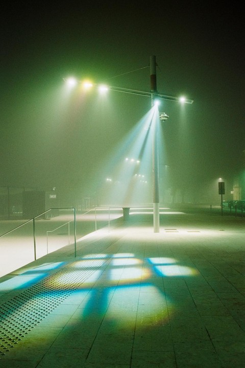 A street light illuminates a foggy street at night, casting colorful reflections on the pavement.