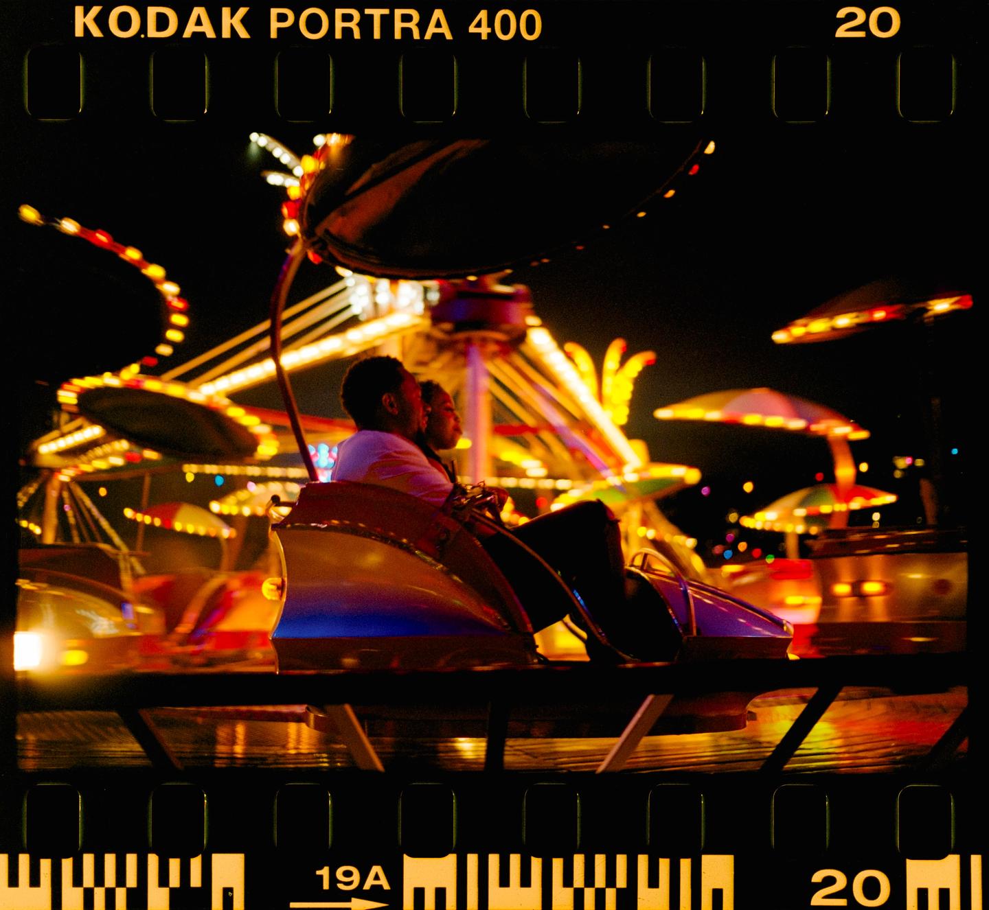 A couple rides a brightly lit carnival ride at night.