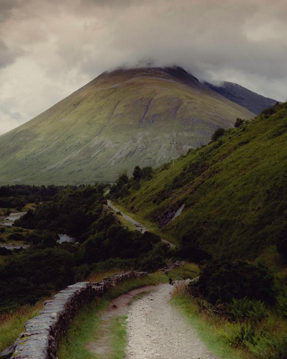 A winding path leads through a valley towards a large mountain partially obscured by clouds.