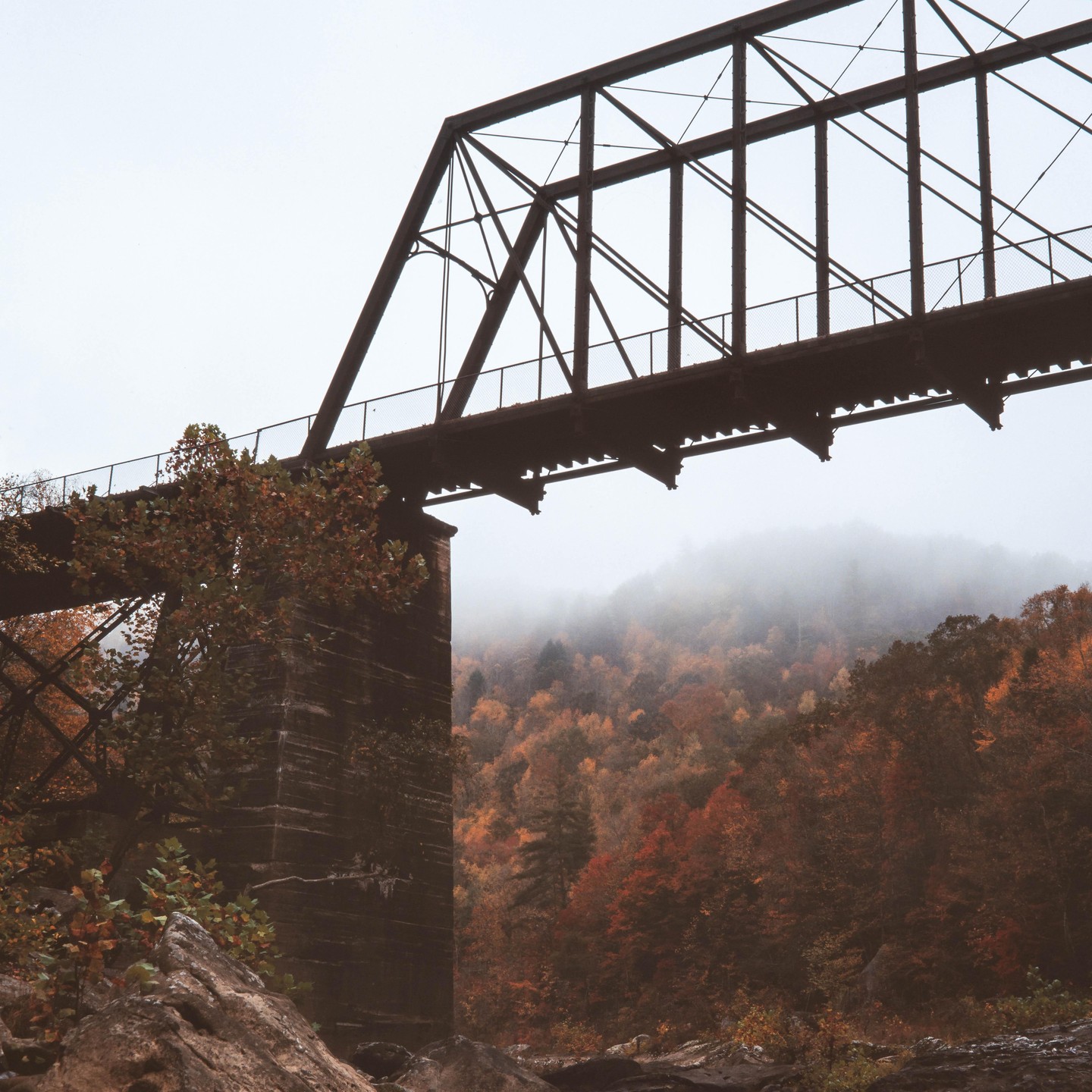 An old railroad bridge spans a valley filled with autumn trees and fog.