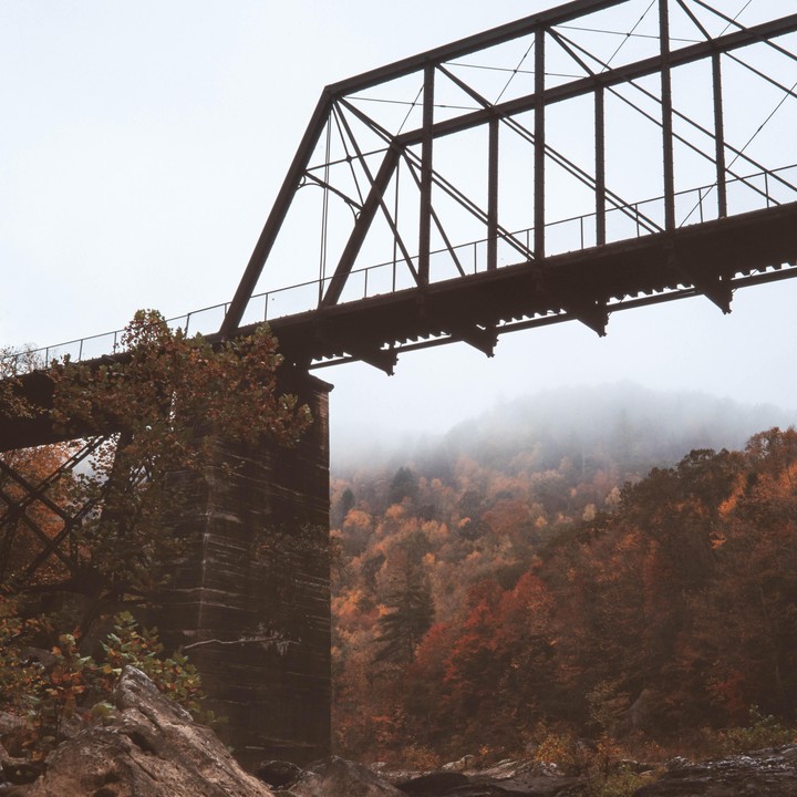 An old railroad bridge spans a valley filled with autumn trees and fog.