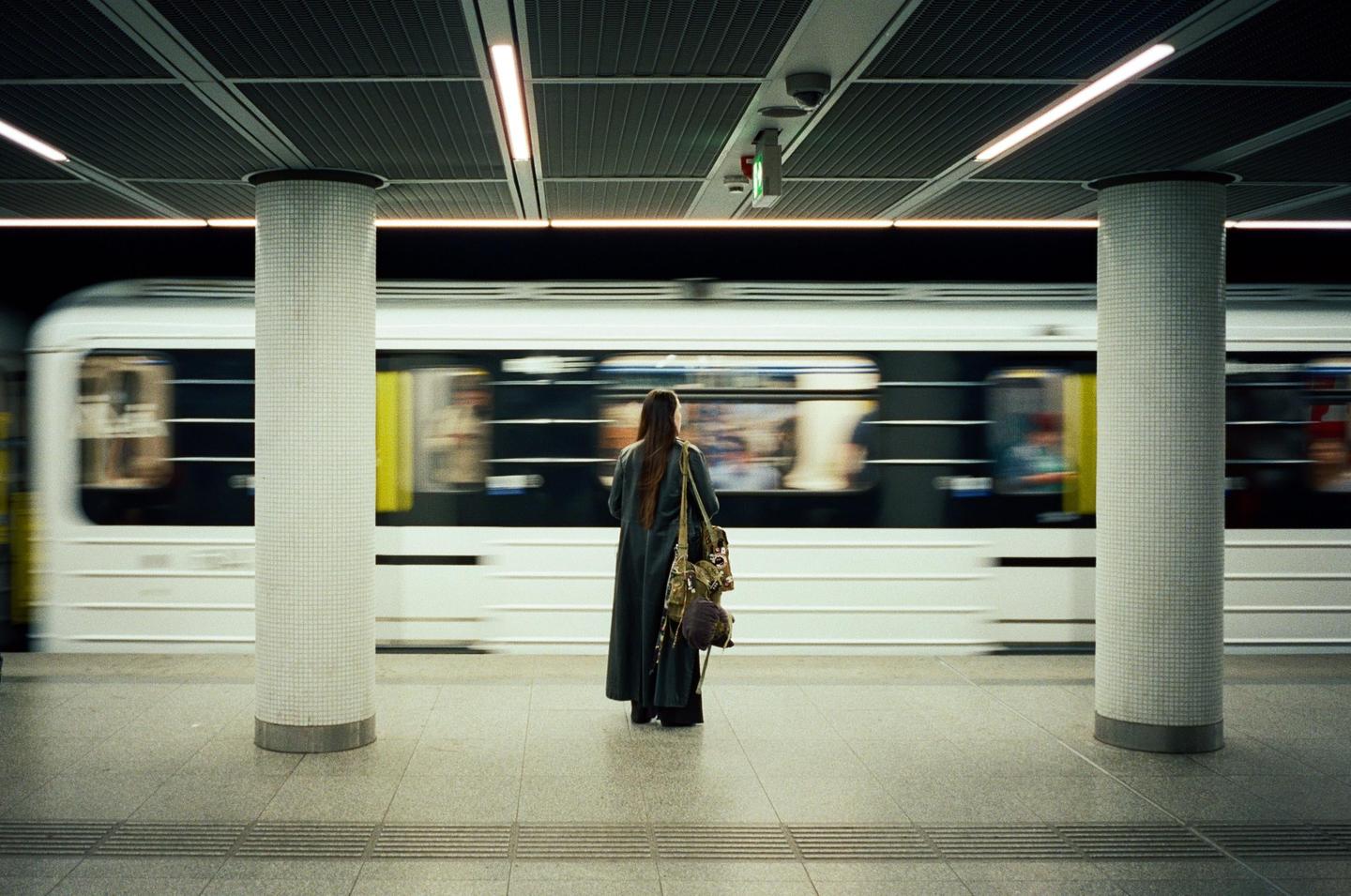 A woman stands on a subway platform as a train passes by.