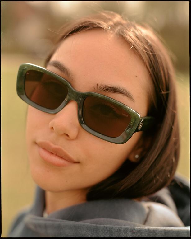 A woman wearing sunglasses looks directly at the viewer.