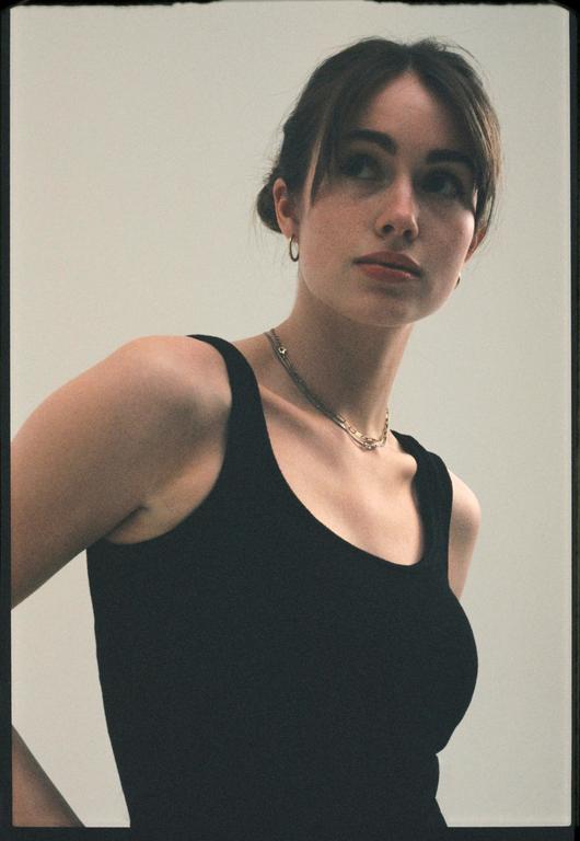 A young woman with her hair pulled back and bangs framing her face looks up and to the right.