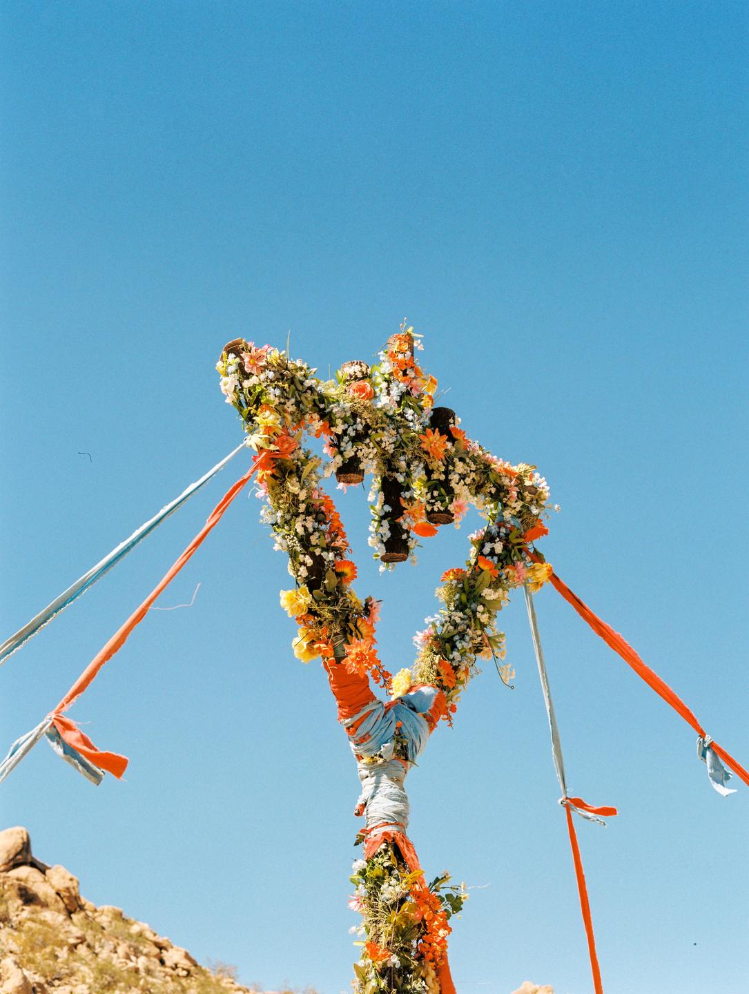 A heart-shaped floral arrangement with ribbons stands against a clear blue sky.