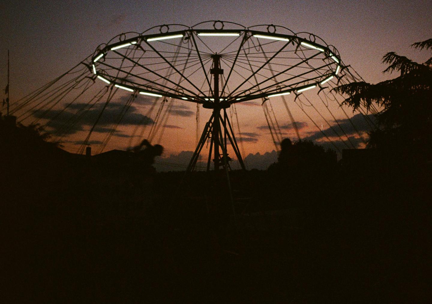A carousel with lights is silhouetted against a sunset sky.