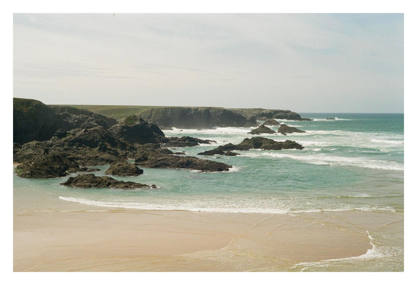 A sandy beach with turquoise water and rocky outcrops is visible under a bright sky.