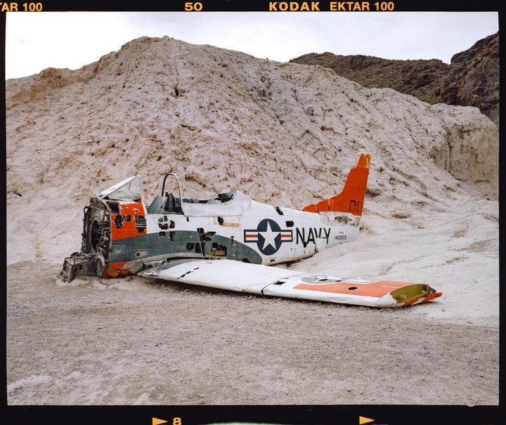 A crashed airplane wreck with "NAVY" written on its side lies in a desert landscape with white hills.