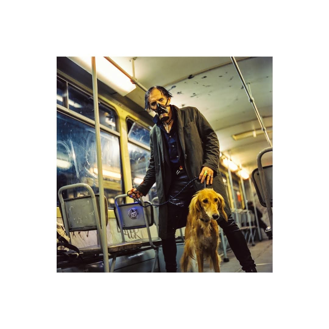 A man wearing a gas mask stands with a dog on a leash inside a tram.