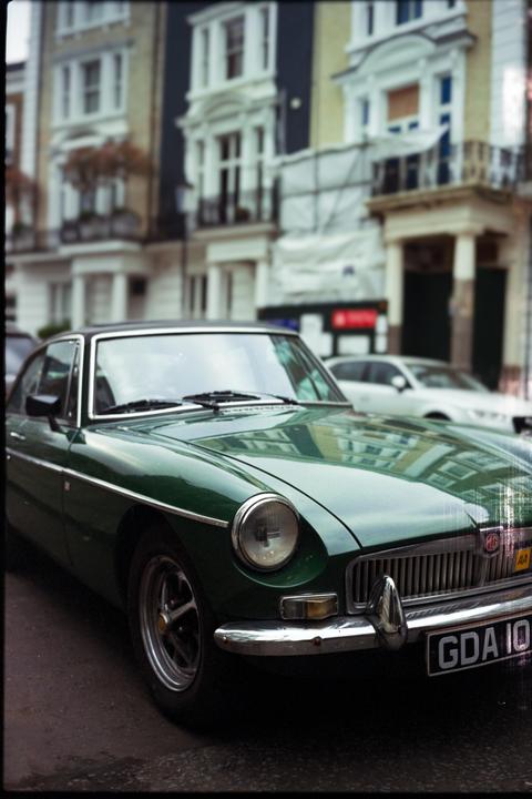 A green vintage car is parked on a street in front of buildings.