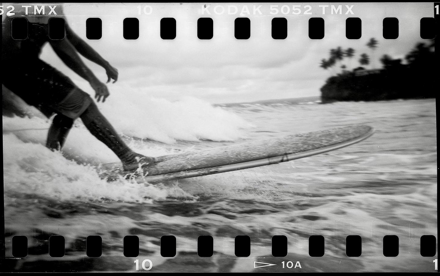 A surfer rides a wave on a surfboard with a tropical island in the background.