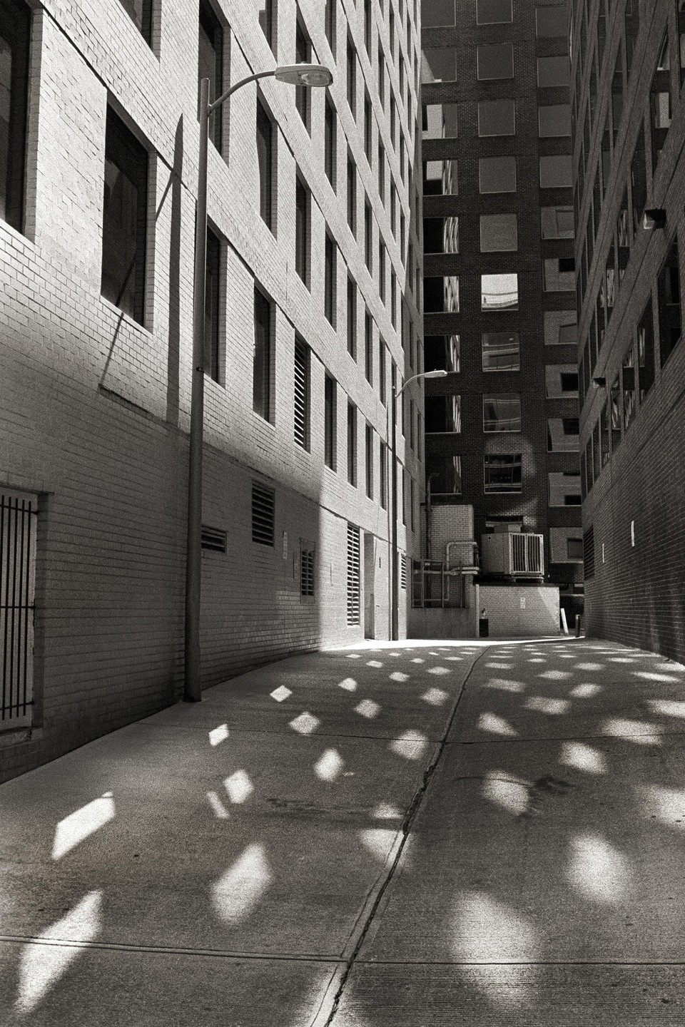 Sunlight casts square patterns on the ground of a narrow alleyway between two tall buildings.