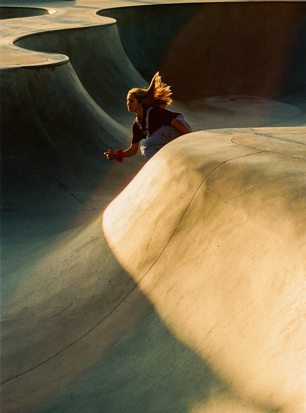 A woman with long hair skates in a concrete skatepark during golden hour.