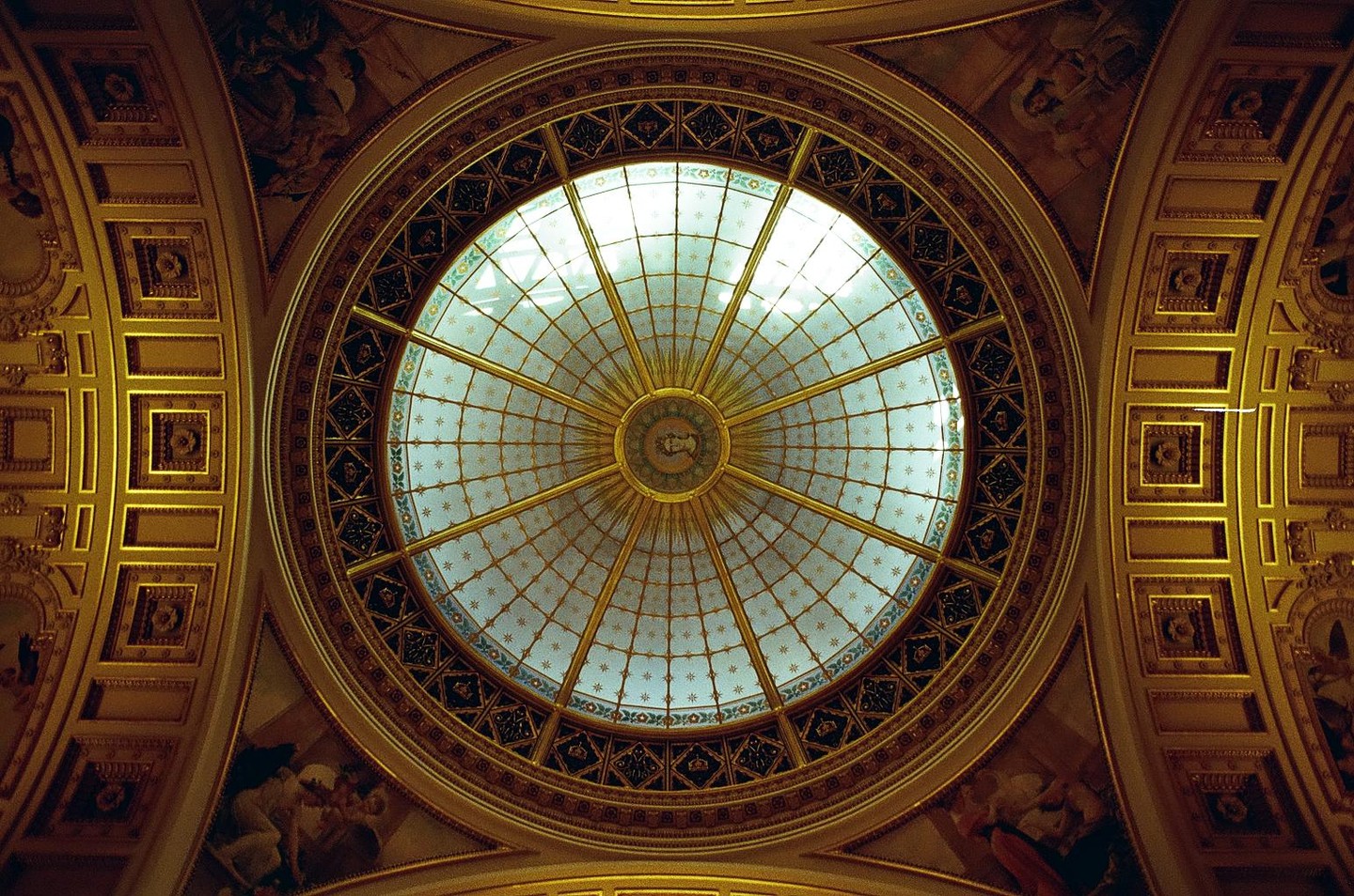 A large, ornate, circular stained glass ceiling is surrounded by gold trim and painted murals.