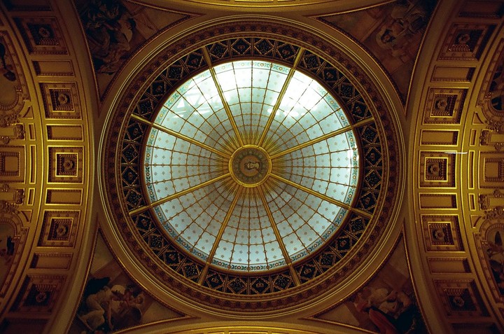A large, ornate, circular stained glass ceiling is surrounded by gold trim and painted murals.