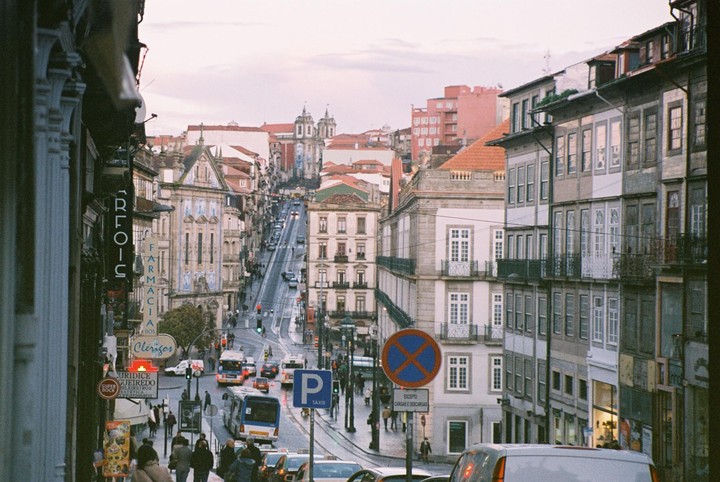 A street in Porto is filled with cars and people at dusk, with buildings lining both sides of the road.