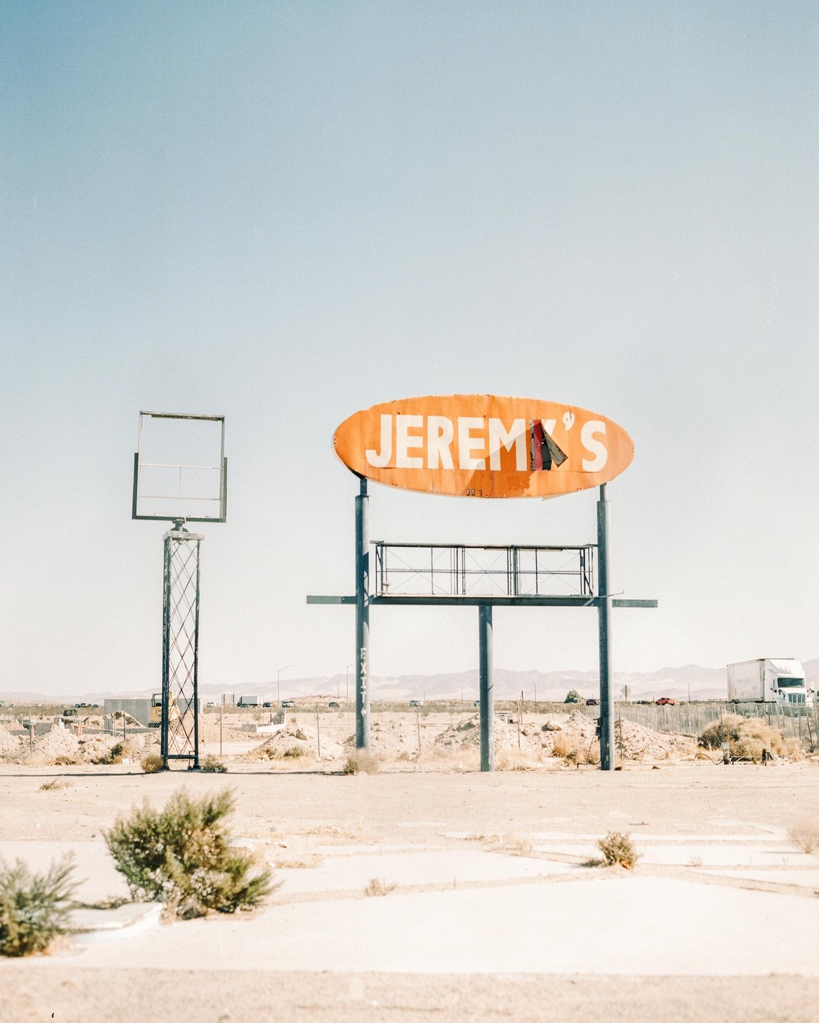 An orange sign for "Jeremy's" stands in a desert landscape next to an empty billboard frame.