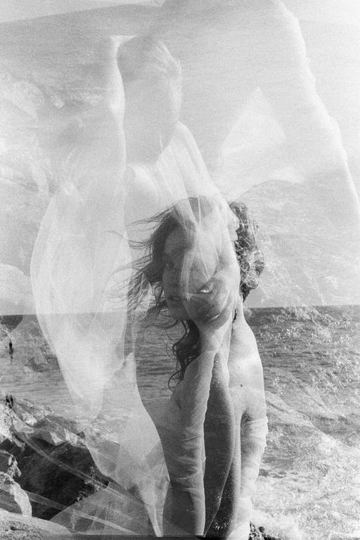 A double exposure shows a woman with long hair covering her face, superimposed over a rocky coastline with crashing waves.