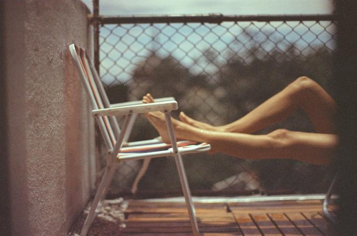 A person's legs and feet are visible as they relax in a folding chair on a balcony.