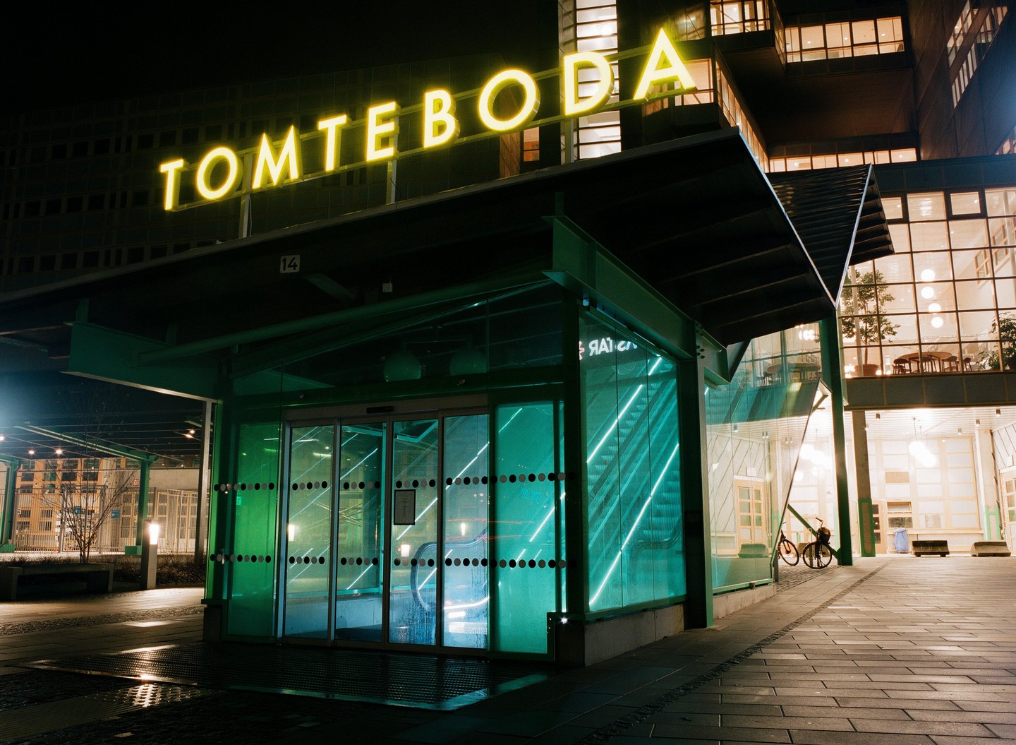 A building with a neon sign that reads "TOMTEBODA" is visible at night.