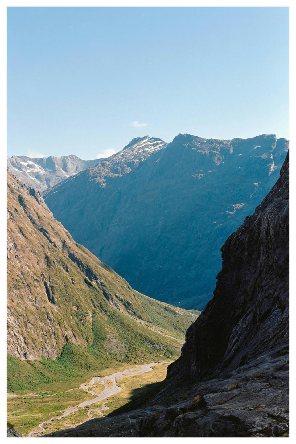 A valley with a river and mountains with snow-capped peaks is visible under a clear sky.