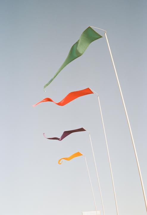 Four colorful flags on poles wave against a clear sky.