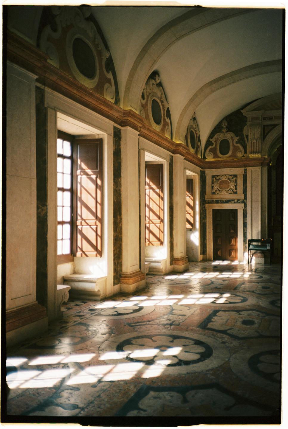 Sunlight streams through windows, casting patterns on the ornate floor of a long hallway.