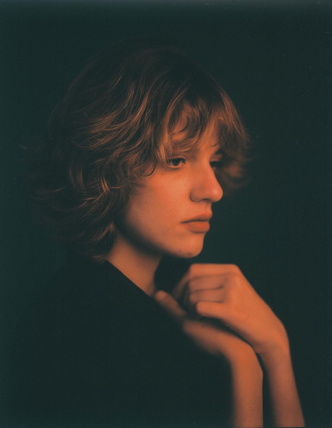 A woman with short hair looks down and to the right, with her hands clasped in front of her.