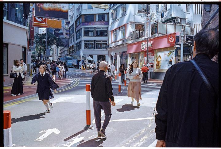 A young woman in a school uniform runs across a busy street in a city.