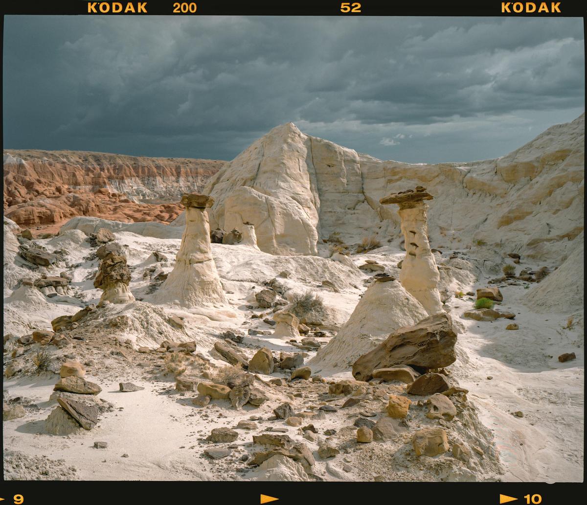 A landscape of white and red rock formations is visible under a cloudy sky.