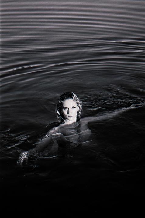 A woman with wet hair is swimming in dark water, looking directly at the viewer.