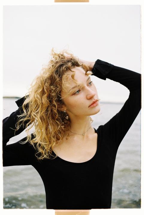 A woman with curly hair looks away from the camera with her hands in her hair.