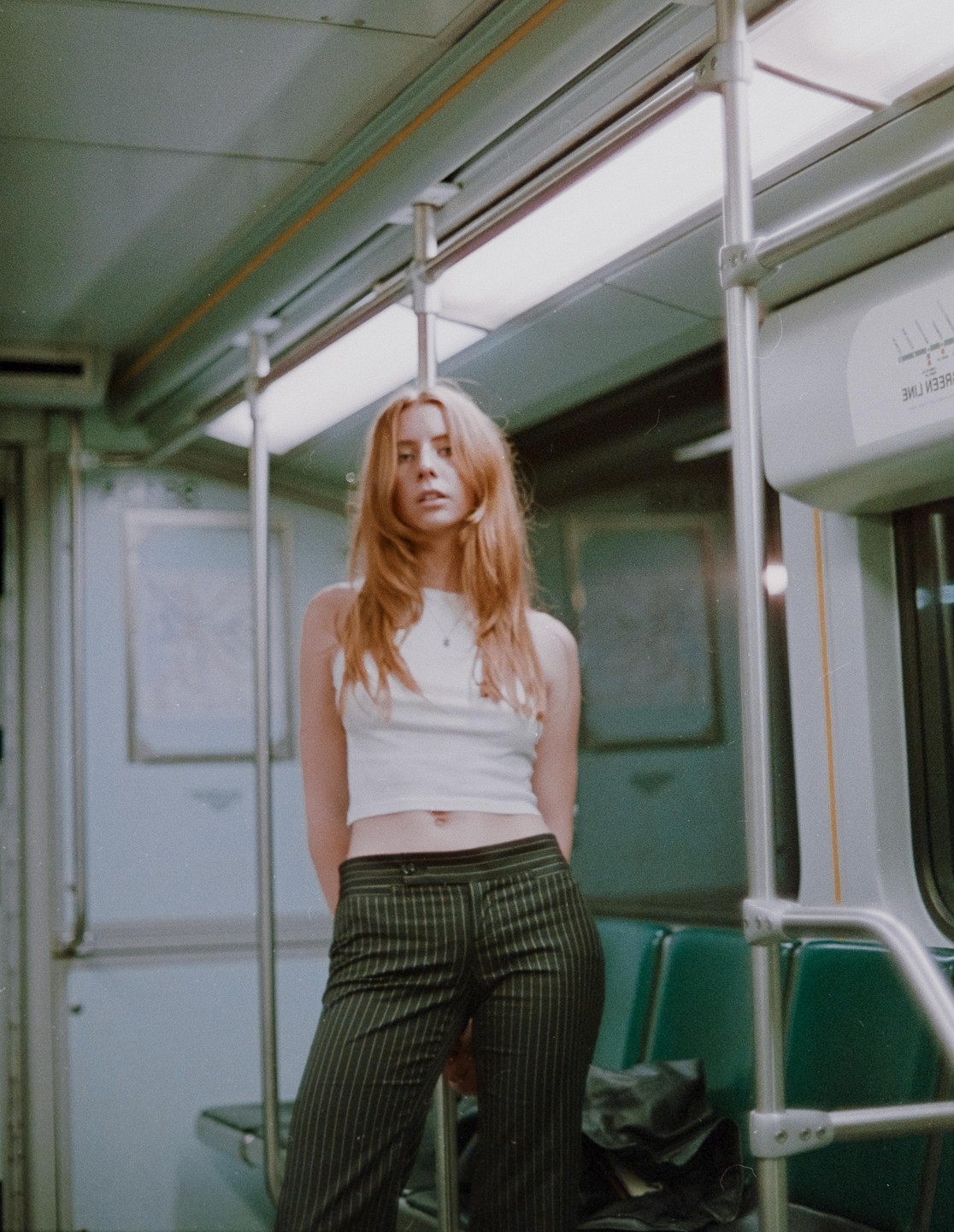 A woman with long red hair stands in a subway car.