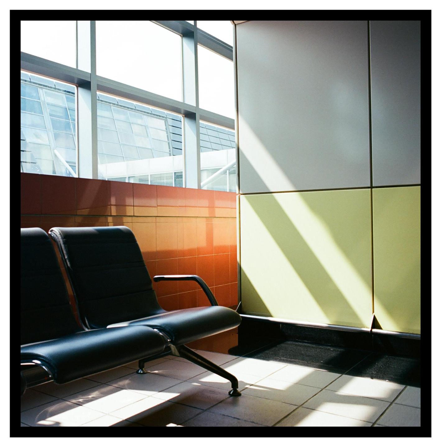 Sunlight streams through a large window onto a black waiting room bench and a tiled wall.