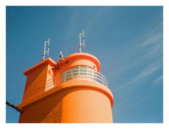 An orange building with a balcony and antennas on top stands against a clear blue sky.