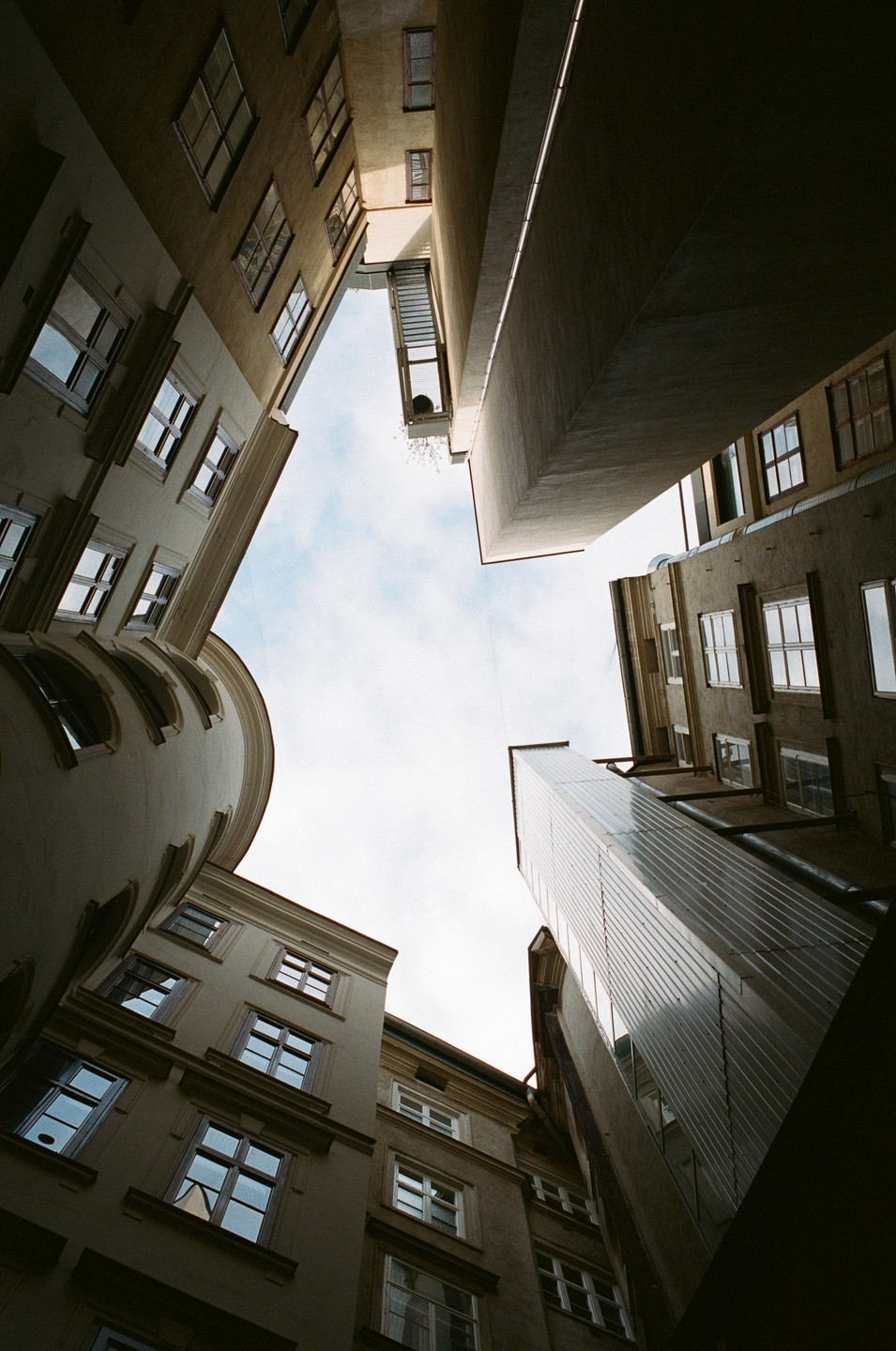 A low-angle view shows the sky framed by tall buildings with many windows.