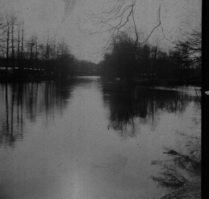 A river flows through a wooded area with bare trees reflected in the water.