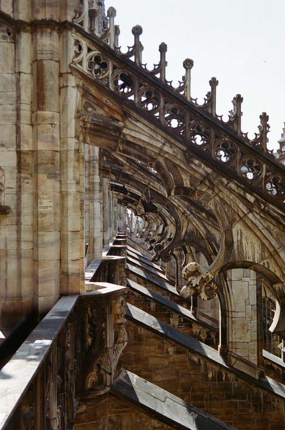 A detailed view of the ornate gothic architecture of the Milan Duomo, showing flying buttresses and decorative elements.