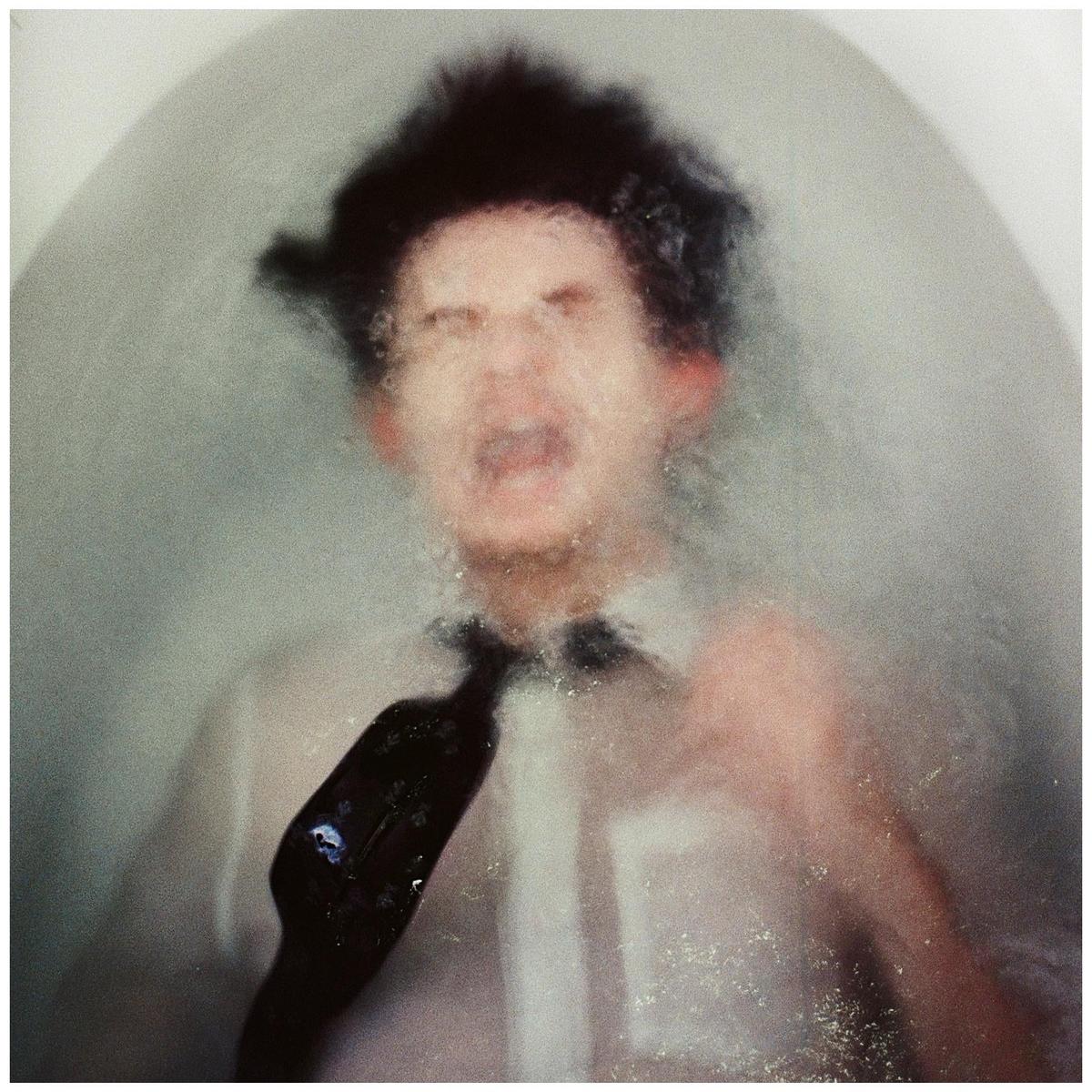 A man in a white shirt and black tie is submerged in water, with his face distorted by the water.