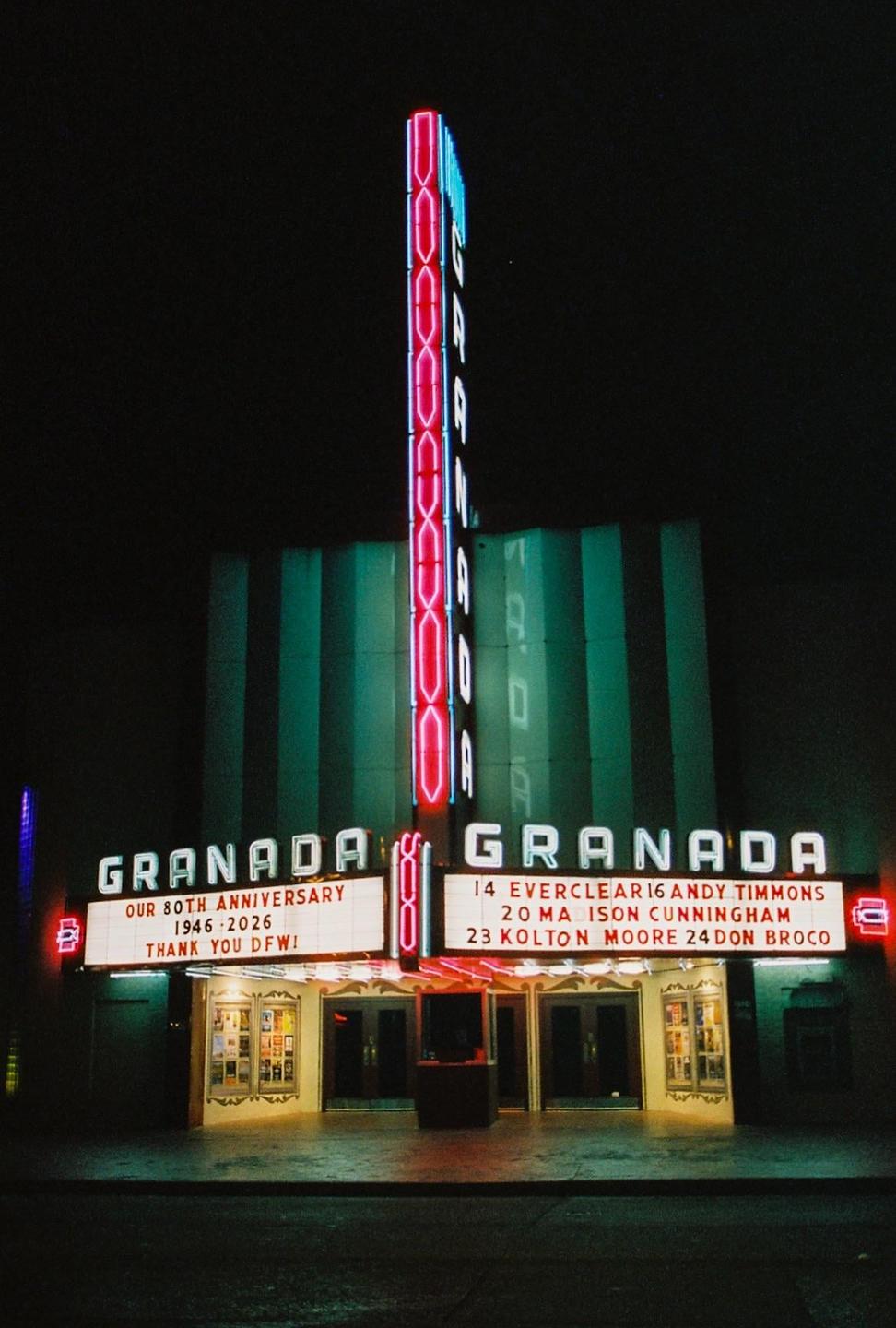 A movie theater with a large neon sign and marquee is illuminated at night.