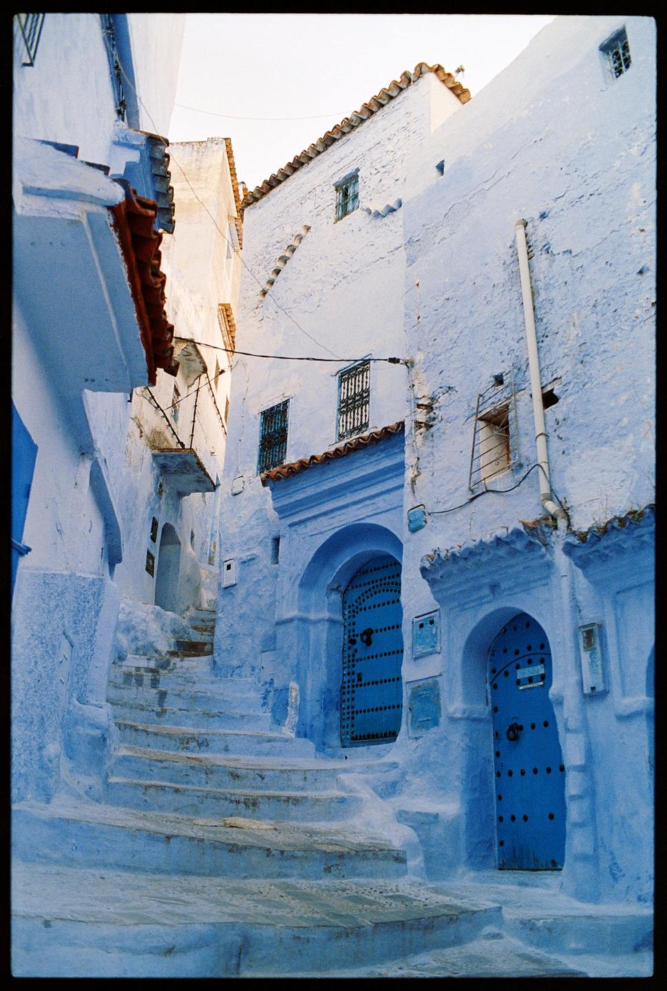 A narrow alleyway with steps is lined with blue-painted buildings and arched doorways.